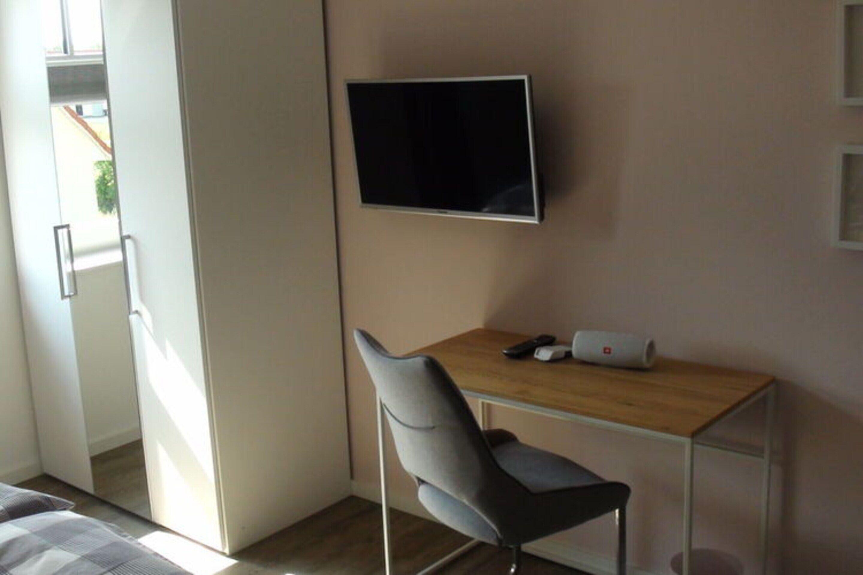 Una camera d'albergo moderna con un letto, una scrivania con una sedia, una televisione a schermo piatto montata a parete e un piccolo tavolino con un portatile e un telefono.