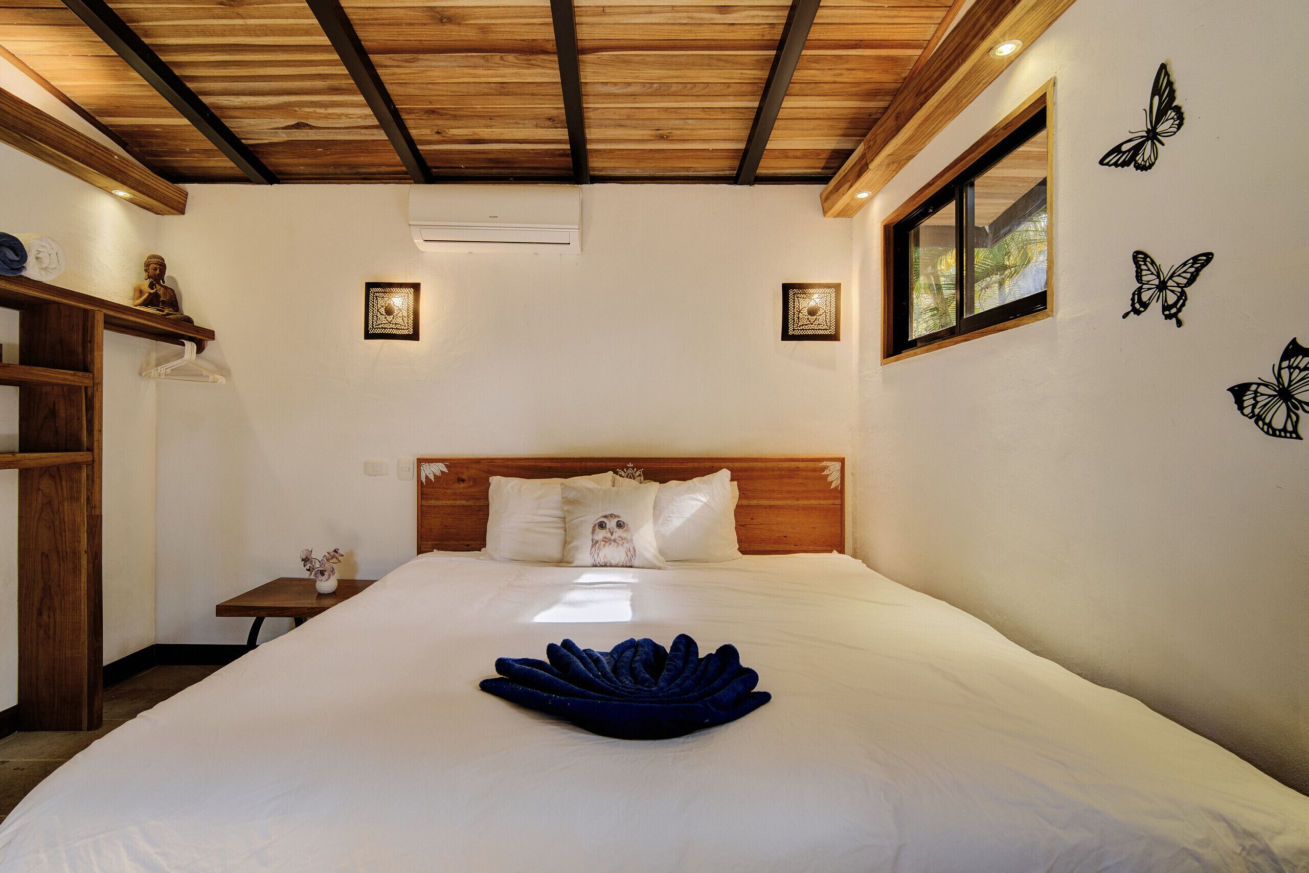 A neatly made bed with a blue towel centerpiece, wooden headboard, and butterfly wall decals.