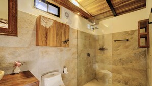 Een badkamer met een houten wastafelmeubel, toilet, een douchecabine van glas en een decoratief wandobject.