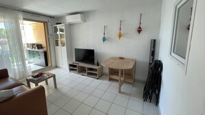 A living room with a TV, a wooden table, a sofa, and a sliding glass door leading to a balcony.