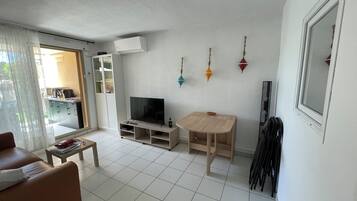 Un salon comprenant un téléviseur, une table en bois, un canapé et une porte-fenêtre coulissante donnant sur un balcon.