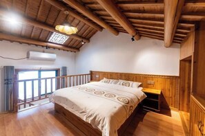 Un dormitorio con piso de madera, una cama, un tragaluz y techo de madera.