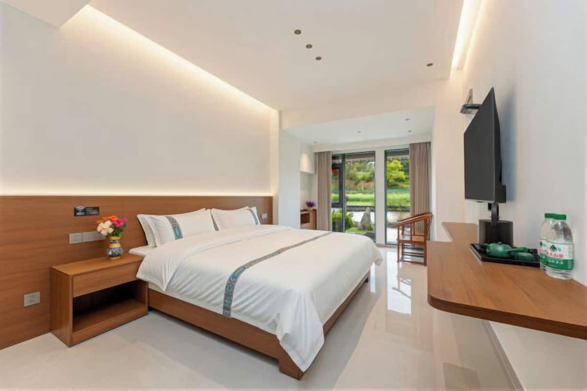 Une chambre d’hôtel moderne dotée d’un grand lit, d’une table de chevet en bois, d’un téléviseur à écran plat et offrant une vue sur l’extérieur.
