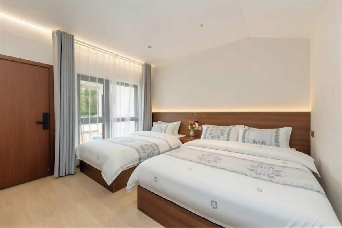 Une chambre d’hôtel avec deux lits, une porte en bois et une grande fenêtre avec des rideaux.