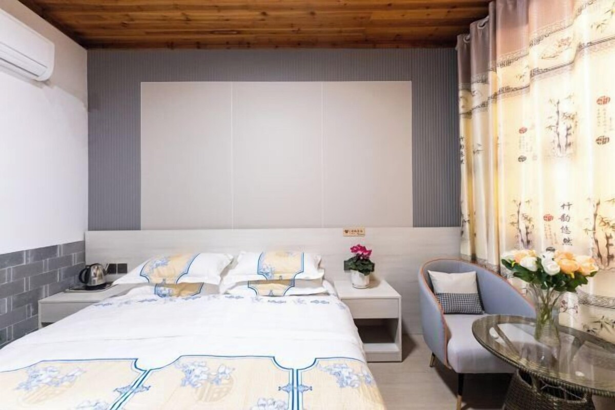 Un dormitorio con cama, mesita de noche, silla y una pequeña mesa con flores.