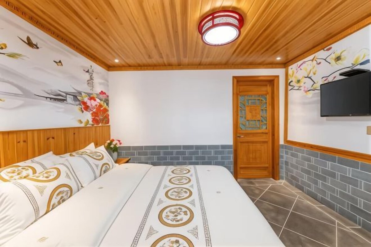 Un dormitorio con cama, techo de madera, televisión y una puerta con panel decorativo.