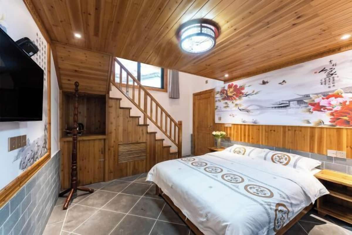Une chambre avec un lit, un escalier en bois et un mur orné d’une fresque florale.