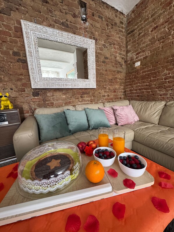 A cozy living room with a brick wall, a large mirror, a beige sofa, and a breakfast setup on a wooden table.