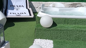 Un'area benessere con vasca idromassaggio, prato sintetico ed elementi decorativi bianchi.