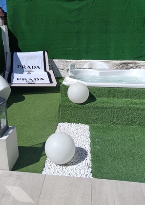 Un espacio de spa con jacuzzi, césped artificial y elementos decorativos blancos.