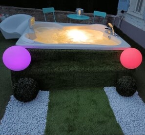 Un jacuzzi iluminado, rodeado de césped artificial y guijarros blancos.