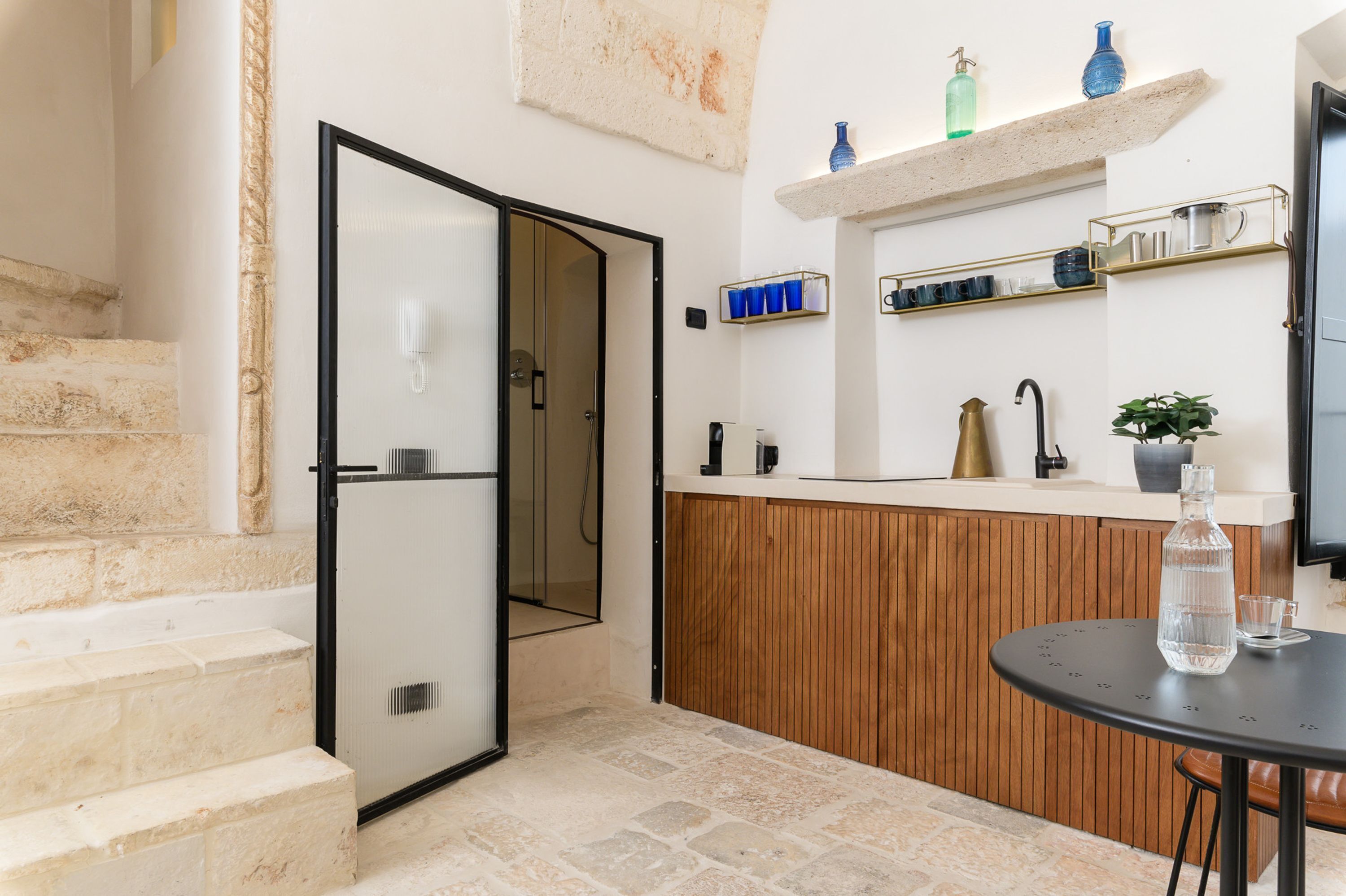 A modern kitchen with a wooden counter, a black table with a bottle, and a TV on the wall.
