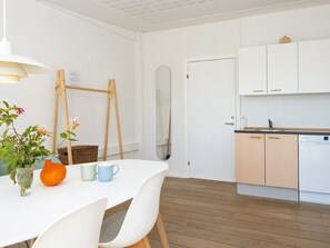 A modern kitchen with white cabinets, a wooden floor, and a dining area with a white table and chairs. - 10 Person Holiday Park Home in Ulfborg (Ulfborg)