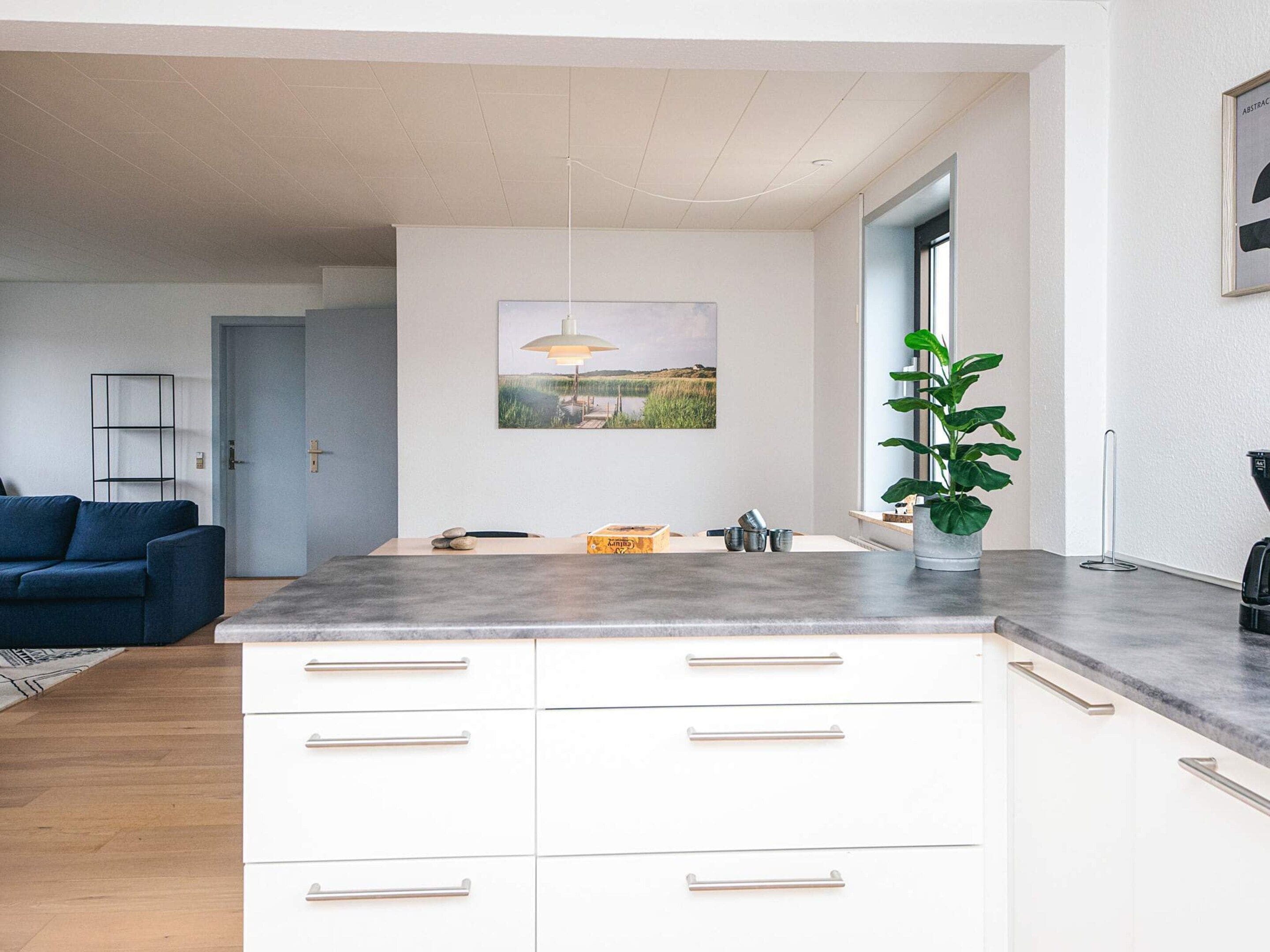 Una cocina moderna con armarios blancos, encimera gris y un área de comedor con sofá azul.