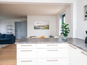 A modern kitchen with white cabinets, a grey countertop, and a dining area with a blue sofa.