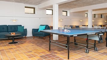 Una mesa de ping pong en un espacio común con suelo de baldosas, sofás y mesas.