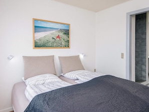 A bedroom with a bed, two pillows, a wall-mounted picture, and a door with a view. - 10 Person Holiday Park Home in Ulfborg (Ulfborg)