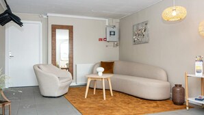 A modern living room with a beige sofa, a round coffee table, and a chair. There is a radiator, a power outlet, and a framed picture on the wall. - 10 Person Holiday Park Home in Ulfborg (Ulfborg)