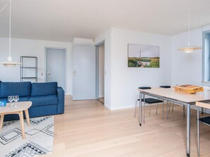 A modern living room with a blue sofa, a dining table, and a painting on the wall.