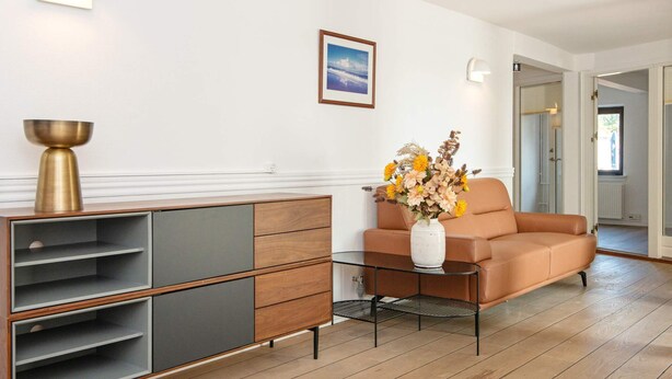 A modern living room with a sofa, a glass coffee table, a cabinet, and a vase with flowers. - 10 Person Holiday Park Home in Ulfborg (Ulfborg)