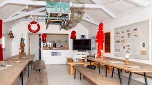 A dining area with wooden tables and benches, a kitchen in the background, and a wall with various photographs and information. - 10 Person Holiday Park Home in Ulfborg (Ulfborg)