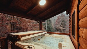 A hot tub in a wooden cabin with a view of autumn trees.
