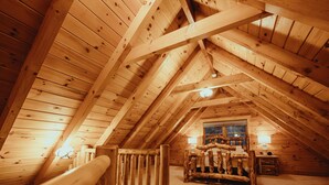 A wooden attic bedroom with a sloped ceiling, a bed with a rustic headboard, and two bedside lamps.