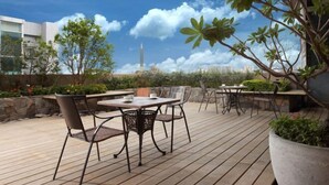 Un patio al aire libre con una mesa y sillas, rodeado de plantas y vistas a una torre distante.
