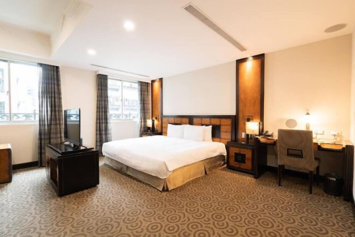 Una habitación de hotel con una cama grande, un escritorio con silla, un televisor y un armario.