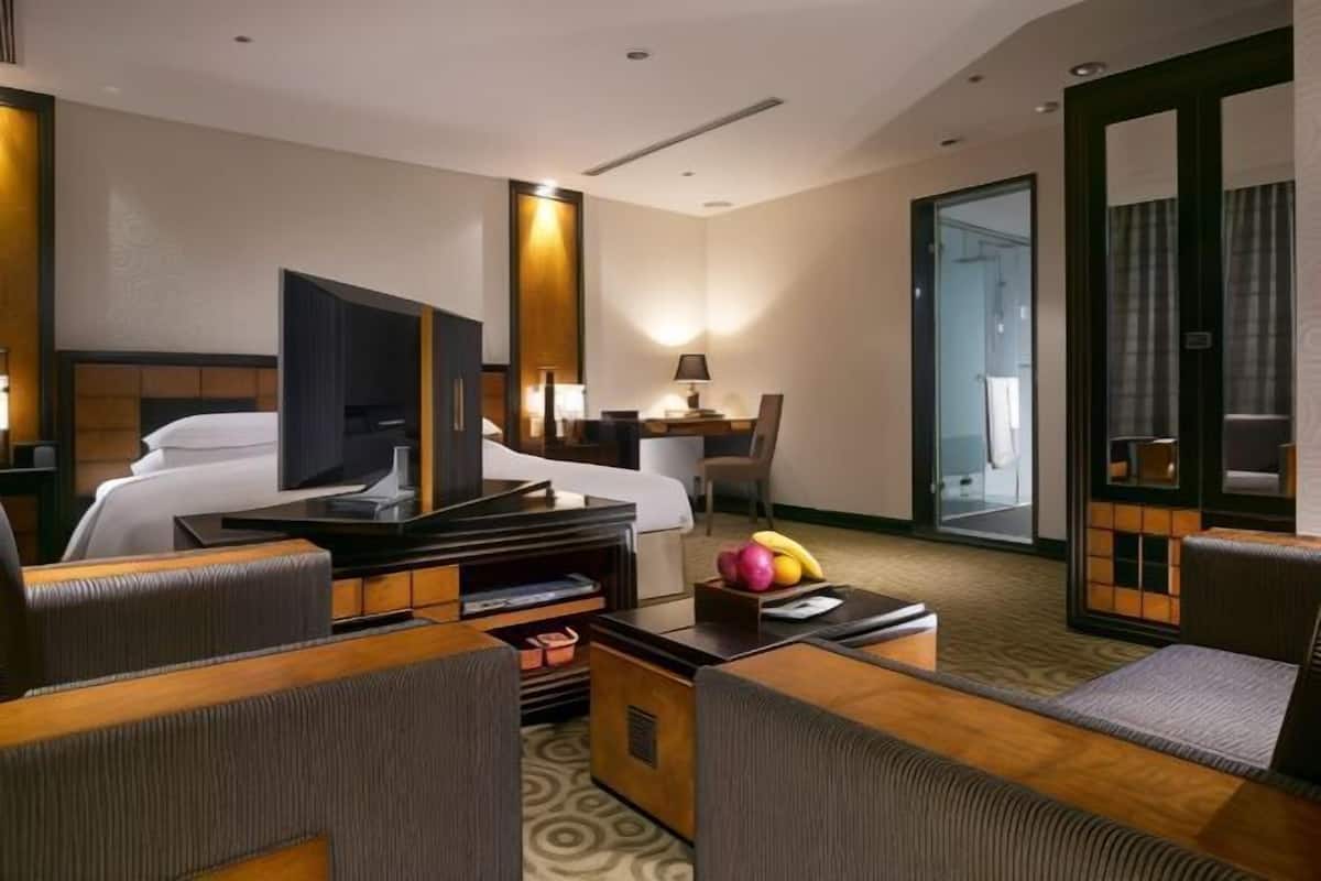 Habitación de hotel con cama, escritorio, silla, televisor y una mesita con fruta.