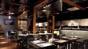Un restaurante con mesas dispuestas para comer, una zona de bar y una cocina al fondo.