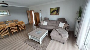 A modern living room with a grey sofa, a coffee table, and a dining area with wooden chairs and a table. - Holiday Apartment Falkenlay (Bad Bertrich)