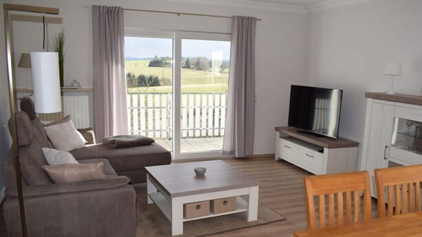 A living room with a sofa, a coffee table, a TV, and a dining table. - Holiday Apartment Falkenlay (Bad Bertrich)