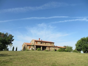 A stone house with a tiled roof, surrounded by a grassy field and trees.