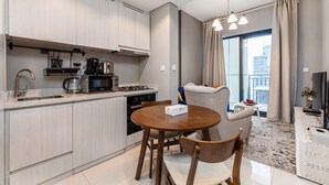 A modern kitchen with a dining area, including a round table and chairs, a coffee maker, and a microwave. - Zada Tower 1BR (Dubai)