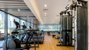 A modern gym with treadmills, weight machines, and a large window offering a view of the city. - Zada Tower 1BR (Dubai)