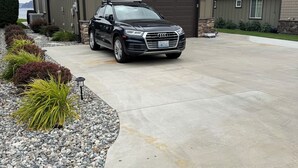 Una casa moderna de dos pisos con garaje, un camino de entrada y una camioneta SUV negra estacionada al frente.