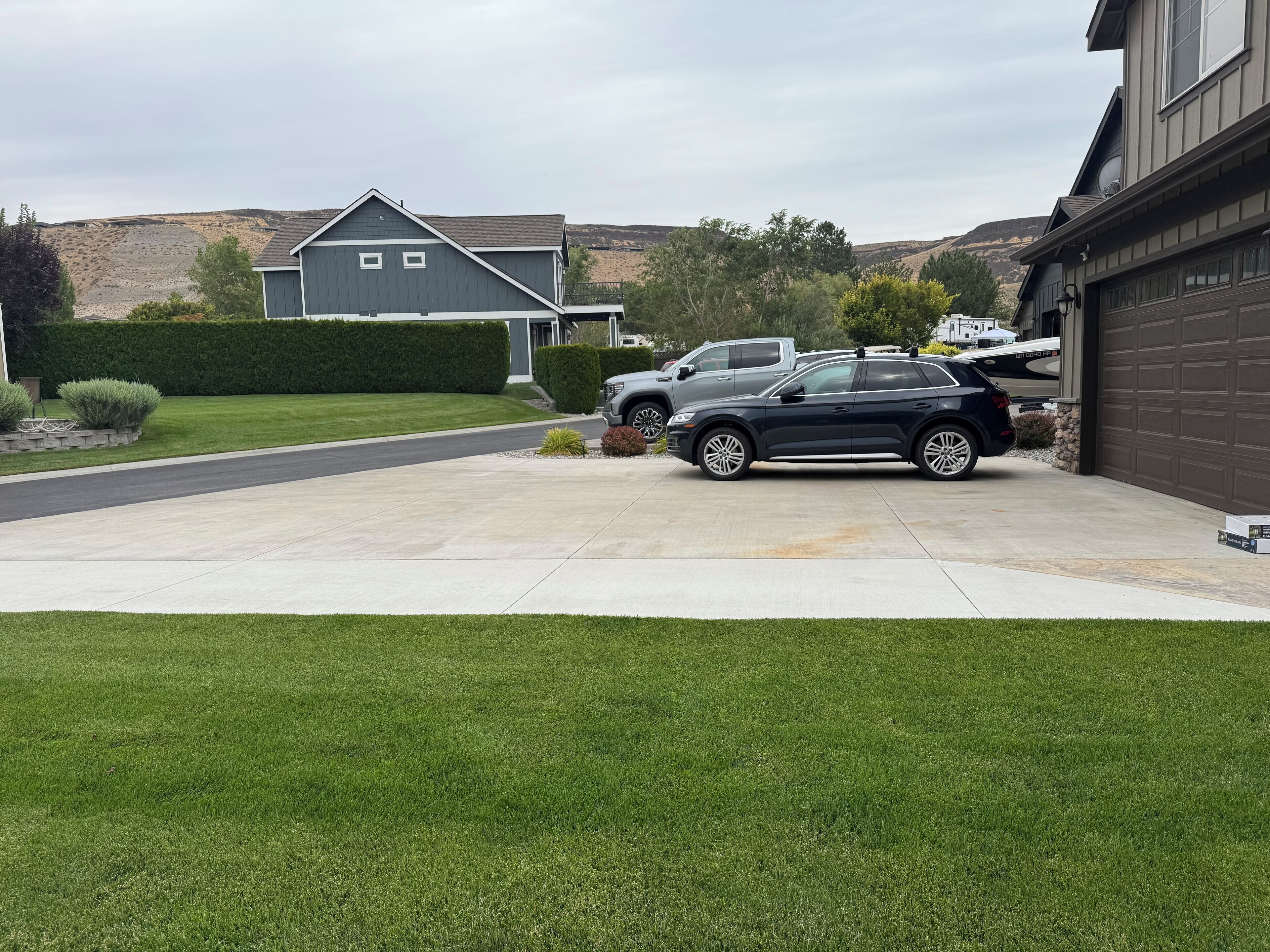 A residential driveway with two cars parked, a garage, and a well-maintained lawn.