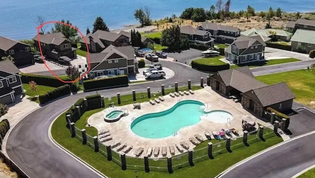 Vista aérea de una zona residencial con una gran piscina rodeada de casas, una carretera curva y una masa de agua al fondo.