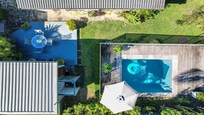 Oversigtsbillede af en bolig med swimmingpool, terrasse med bord og stole samt et overdækket udendørs område.