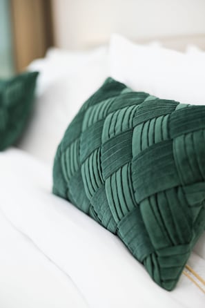 Un gros plan d’un coussin vert tissé posé sur un lit blanc.