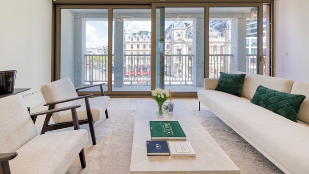 Ein modernes Wohnzimmer mit großem Fenster, einer Couch, einem Couchtisch und zwei Sesseln.