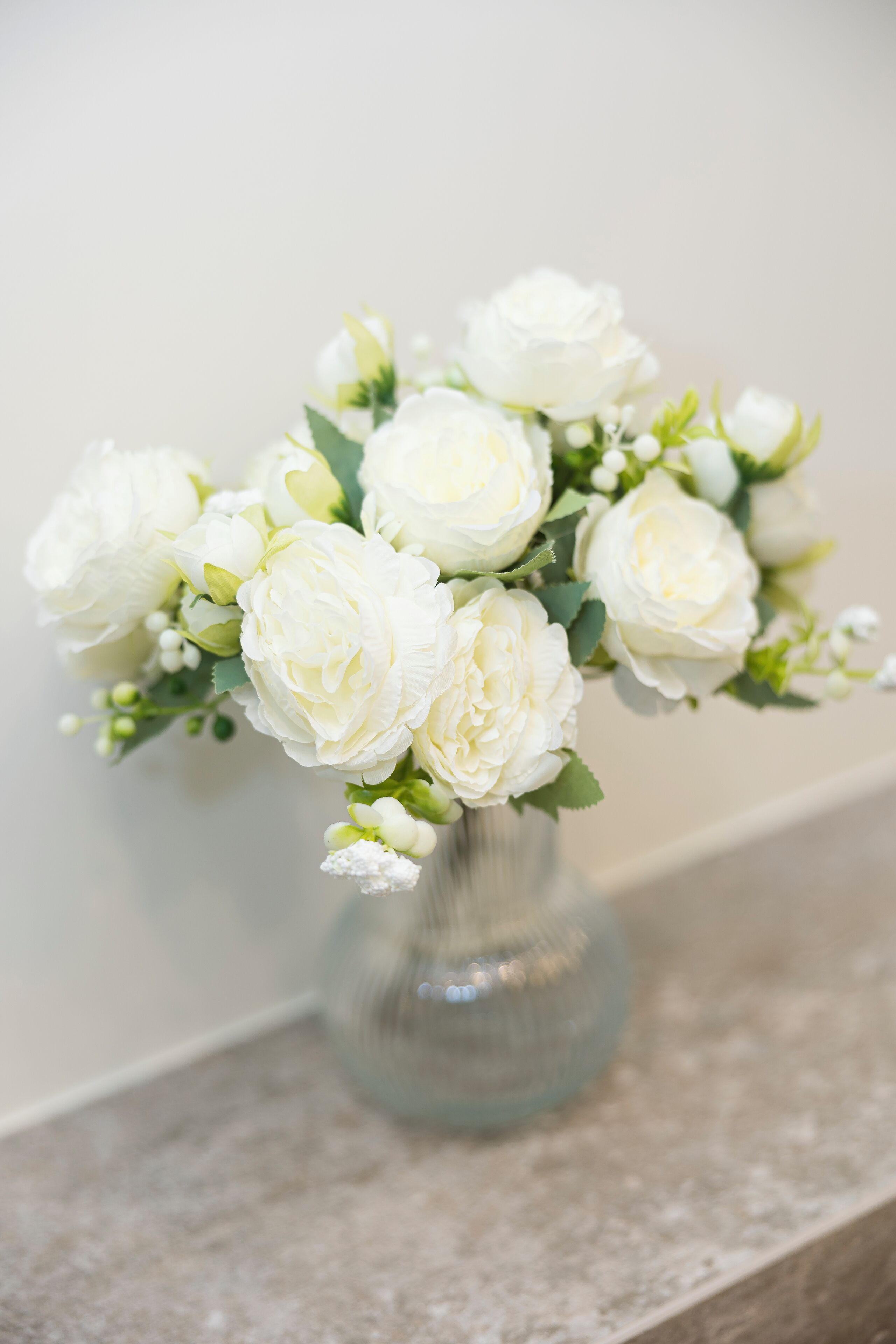 A clear glass vase with white flowers on a marble countertop.