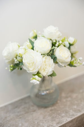 Un vase en verre transparent contenant des fleurs blanches, posé sur un comptoir en marbre.