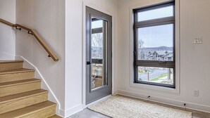 Una escalera de madera conduce a un rellano con una puerta y un ventanal grande.