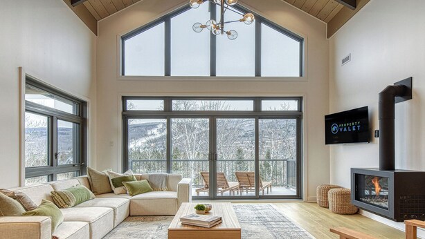 Un salón amplio con techo alto, ventanas grandes, un sofá acogedor, una mesa de centro de madera y una chimenea.