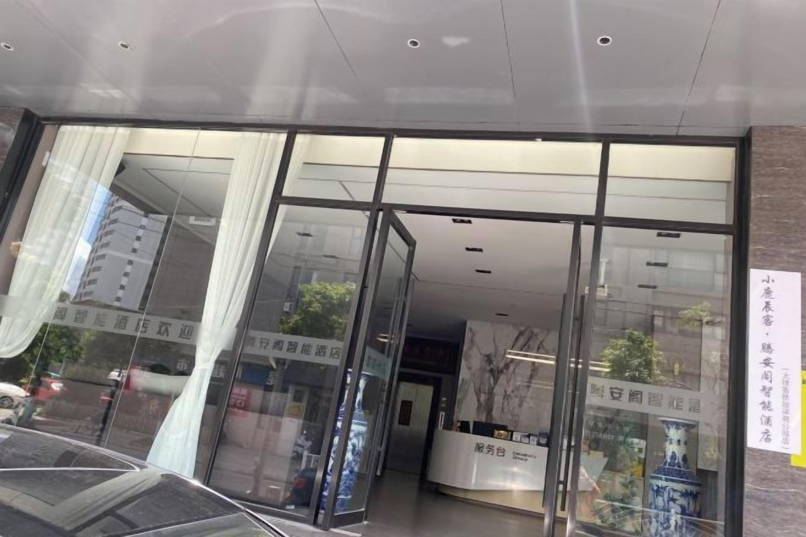 A hotel entrance with glass doors, a reception desk, and a sign with text.