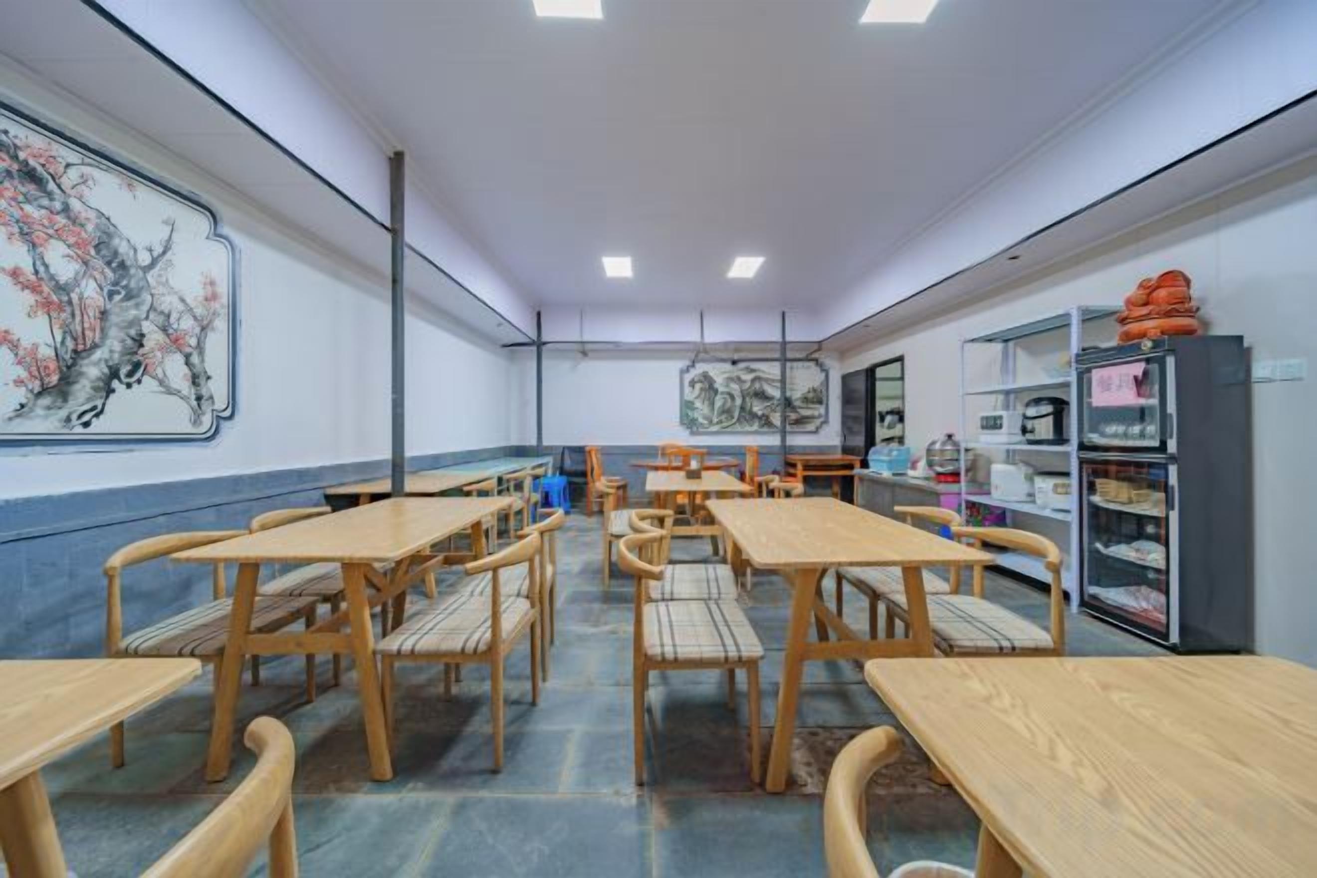 Une pièce comprenant plusieurs tables et chaises en bois, un grand tableau au mur et des étagères remplies d’objets sur le côté droit.