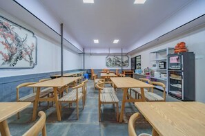 A room with multiple wooden tables and chairs, a large painting on the wall, and shelves with items on the right side. - Dali Teng'ange Smart Hotel (Dali High-speed Railway Station) (Dali City)