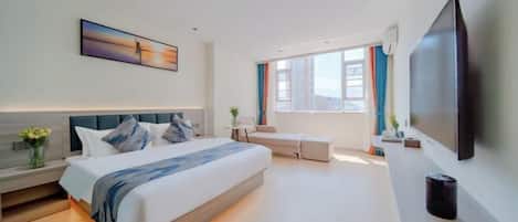A modern hotel room with a large bed, a flat-screen TV, a sofa, and a large window with curtains.